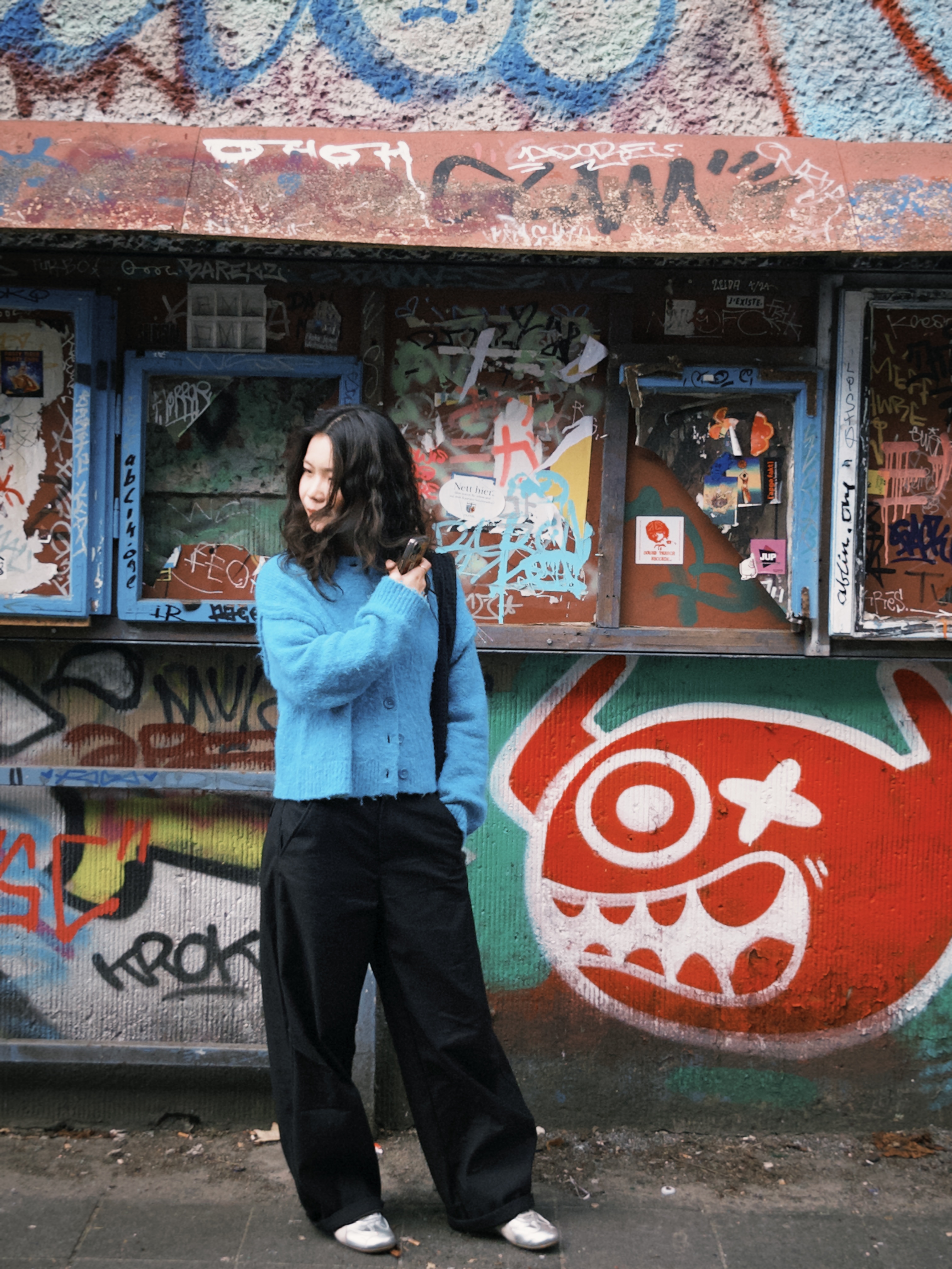Yixuan in a blue sweater standing in front of a colourful graffiti-covered building